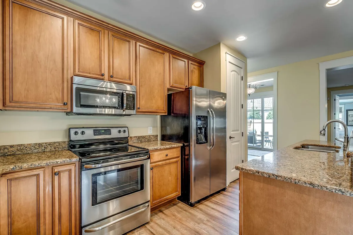 A modern kitchen equipped with stainless steel appliances, granite countertops, and warm wood cabinetry. The space is functional for cooking or entertaining, and opens up to the living and dining areas, reinforcing the open-concept design.
