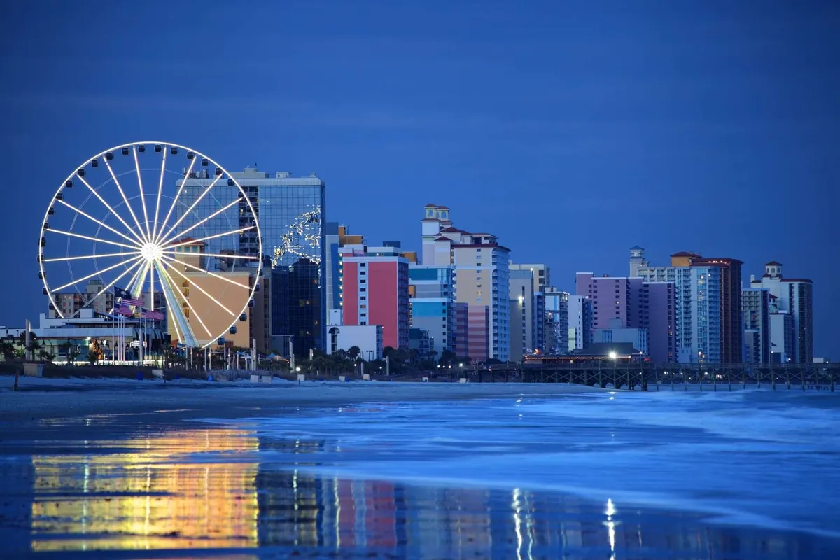 A vibrant Ferris wheel sits along the waterfront, with colorful buildings and shimmering reflections on the water. The festive mood is enhanced by the twilight sky, suggesting an energetic and whimsical evening atmosphere.