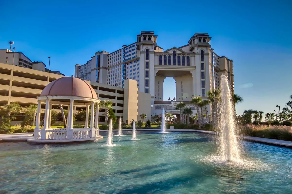 A serene resort exterior featuring a graceful fountain, elegant gazebo, and attractive building architecture, all bathed in sunset light. The scene is ideal for leisurely walks, group gatherings, and relaxation after a day of activities.