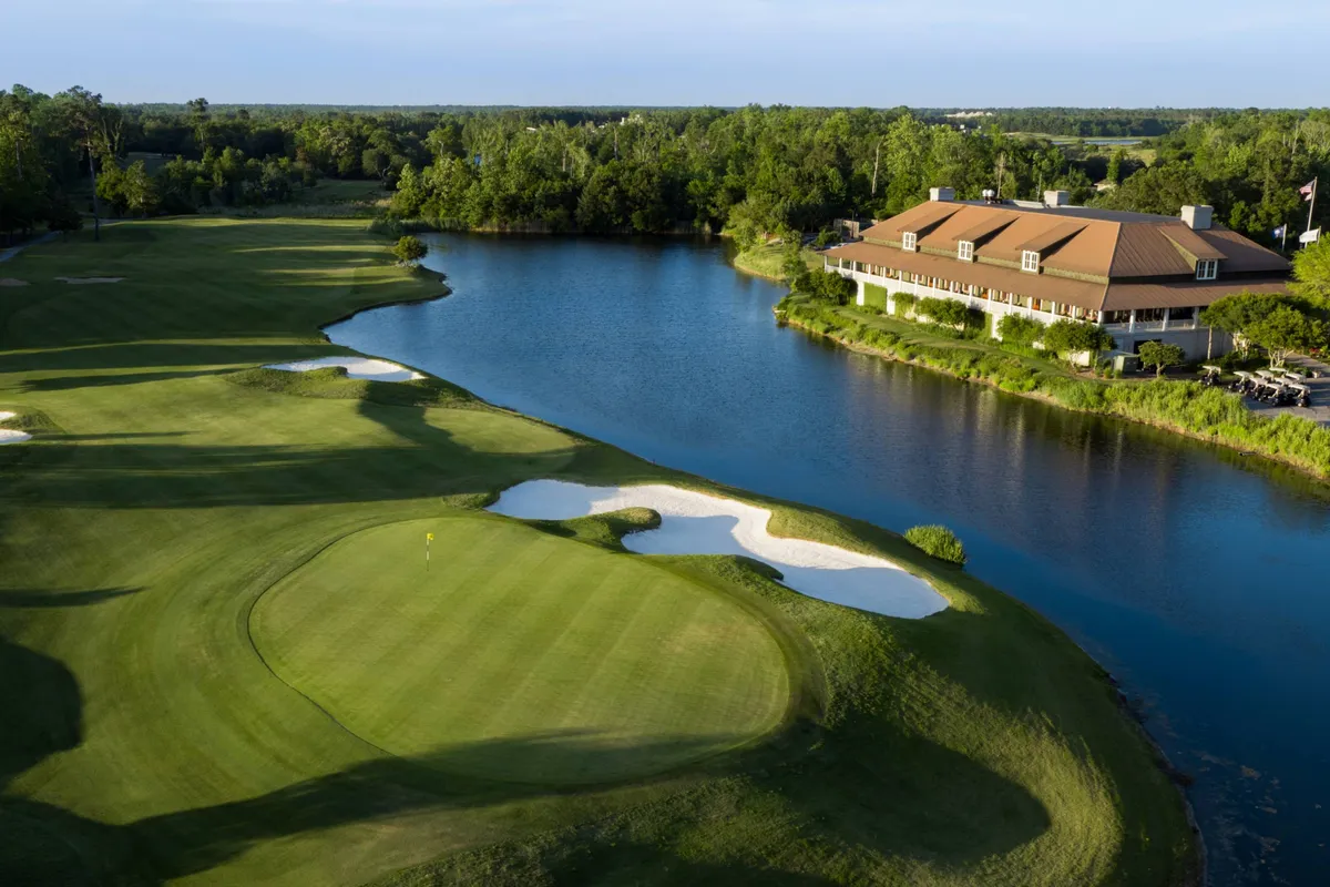 This image features a beautiful golf course with a water body, a clubhouse, and sand traps. The tranquil setting includes lush greenery and the peaceful expanse of the course, ideal for depicting the golf experience near the resort.
