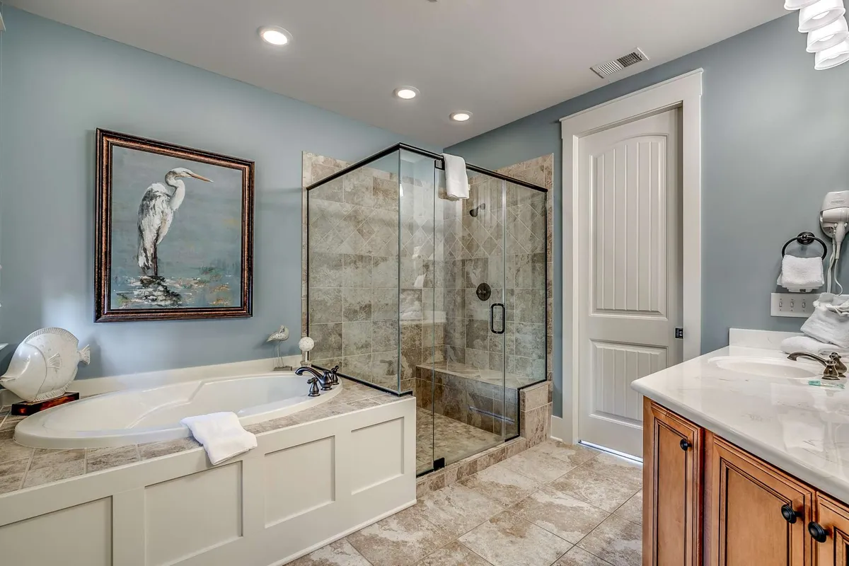 A luxurious bathroom featuring a deep soaking bathtub, glass-enclosed shower, and a framed painting of a heron. The setting is elegant and calming, designed to evoke a spa-like ambiance for unwinding.