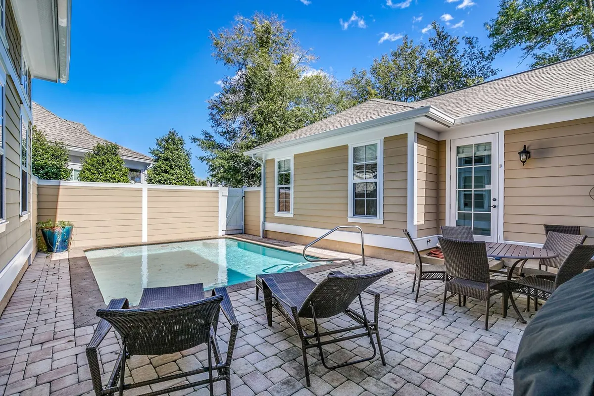 This image features a sparkling swimming pool set amidst an inviting outdoor seating area, with comfortable lounge chairs and lush greenery surrounding the space. The tranquil setting is perfect for relaxation, sunbathing, or social gatherings, with trees providing a sense of privacy and tranquility.