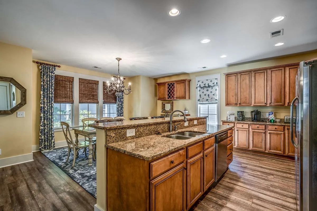 This image shows an interior view featuring a granite countertop, wooden cabinets, and an adjacent dining area with large windows that open views to the outside. The inviting kitchen and dining space suggest smooth indoor-outdoor flow, ideal for preparing meals before enjoying alfresco dining on the patio.