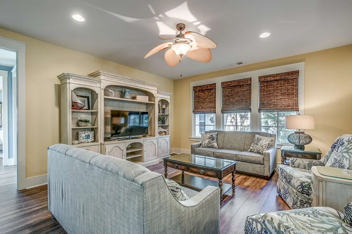 A comfortable living room with a plush sofa, a coffee table at the center, an entertainment unit featuring a TV, and soft window treatments. The room is well-lit with natural light, creating a welcoming and relaxed atmosphere ideal for unwinding, watching TV, or socializing.